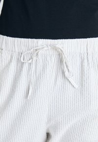 Närbild av vita texturerade byxor med en knytbar midja, bärs tillsammans med en svart topp.