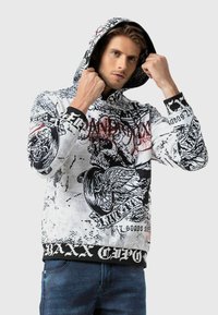 Sweat à capuche en tissu texturé, avec un imprimé graphique noir et blanc présentant des motifs de crâne et d'ailes, et un ourlet en rib d'un noir classique.