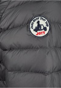 Tejido de chaqueta acolchada gris con un logo bordado redondo que presenta el texto "Just Over The Top" y "JOTT", junto a un gráfico de un patinete.