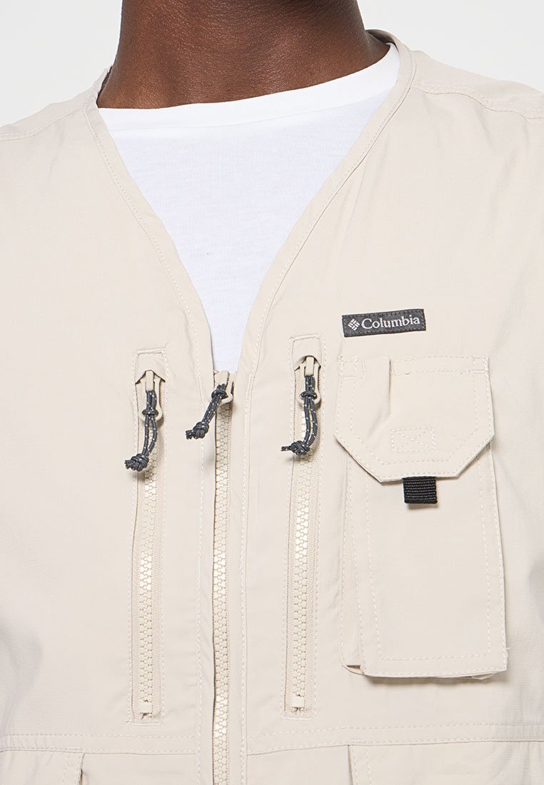 Close-up van een beige Columbia vest met twee verticale ritsborstzakken, een klepzak en een witte ronde hals shirt eronder.