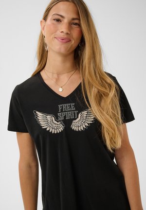 Lachende vrouw met lang blond haar die een zwart V-hals T-shirt draagt met strassvleugels en de tekst "Free Spirit".
