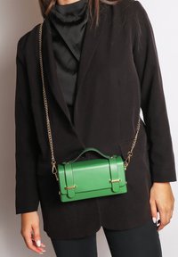 Borsa in eco-pelle verde con design strutturato, accenti in hardware dorato e tracolla a catena removibile. Texture liscia e manici prominenti.