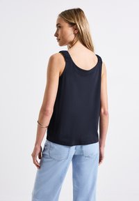 Top nero senza maniche con dettaglio arricciato sulle spalle, realizzato in tessuto morbido. Abbinato a jeans a gamba larga blu chiaro.