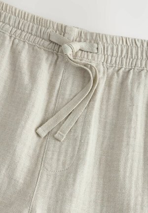 Tessuto a righe herringbone di un beige chiaro con vita elastica e cordoncino, cuciture dettagliate e una tasca laterale.