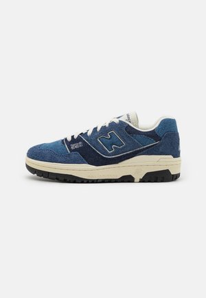 Blauwe suède sneakers met contrasterende marineblauwe panelen, witte veters en een gestructureerde zwarte rubberen zool. Modelnummer "550" op de zijkant weergegeven.