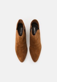 Botines de ante marrón con punta afilada, que cuentan con una cremallera lateral y un forro interno suave. Diseño simple y estilizado.