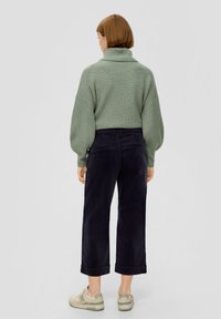 Lichtgroene geribbelde trui met hoge kraag, gecombineerd met donkerblauwe wijde corduroy-broeken en crèmekleurige sneakers. Casual ontwerp en pasvorm.