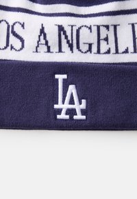 Pletena kapa u tamnoplavoj boji s bijelim prugama. Sadrži tekst "LOS ANGELES" i izvezeni logo "LA" na dnu. Mekana tekstura.