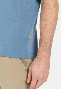 Hellblaues Baumwoll-T-Shirt mit kurzen Ärmeln, versehen mit einem genähten Saum und einem kleinen gelben Markentag an der Seite.