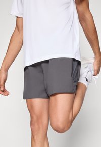 Harmaat urheilushortsit, joissa on sileä pinta, sivutaskut ja rento istuvuus. Yhdistetty löysään valkoiseen paitaan ja tennareihin.