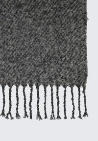 Plaid gris tissé avec un motif texturé, des bords frangés et une apparence douce et duveteuse. Fabriqué en acrylique ou fibres similaires.