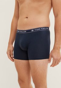 Sötétkék pamut boxer alsónadrág fehér márkázott derékpánttal. Testhezálló fazon, sima érzettel és combközép hosszúsággal.