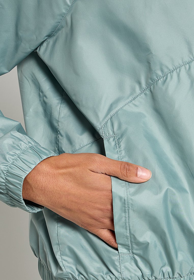 Helle tealfarbene, leichte Jacke mit elastischen Bündchen und Seitentaschen, einer glatten, glänzenden Textur und einem lässigen Schnitt.