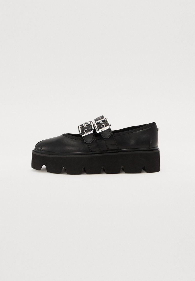 Zapatos de plataforma negros hechos de cuero suave, con doble hebilla plateada y suela de goma texturizada con un borde dentado.