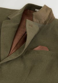 Veste texturée vert olive avec doublure intérieure à motifs marron, col en velours marron et pochette assortie marron.