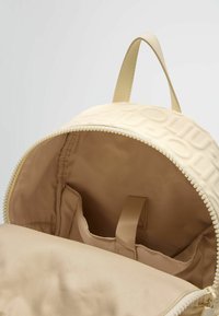 Zaino beige chiaro con esterno testurizzato, chiusura con zip e interno in tessuto dotato di tasche e foderato in beige.