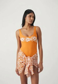 Kollane üheosaline ujumiskostüüm valge lillemustriga, koos sobiva rätikuga, millel on seotud aktsent. Sile tekstuur, sobiv disain.