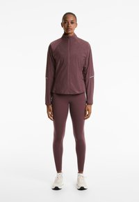 Bordo lagana jakna na zip s mrežastim detaljima, uparena s pripijenim tajicama u istoj boji. Bijeli detalji na rukavima. Bijele tenisice upotpunjuju izgled.