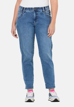 Jeans de mezclilla azul con pierna recta, cinturilla elástica, bolsillos frontales y un ligero desvanecimiento. Combinados con zapatillas grises y calcetines rosas.