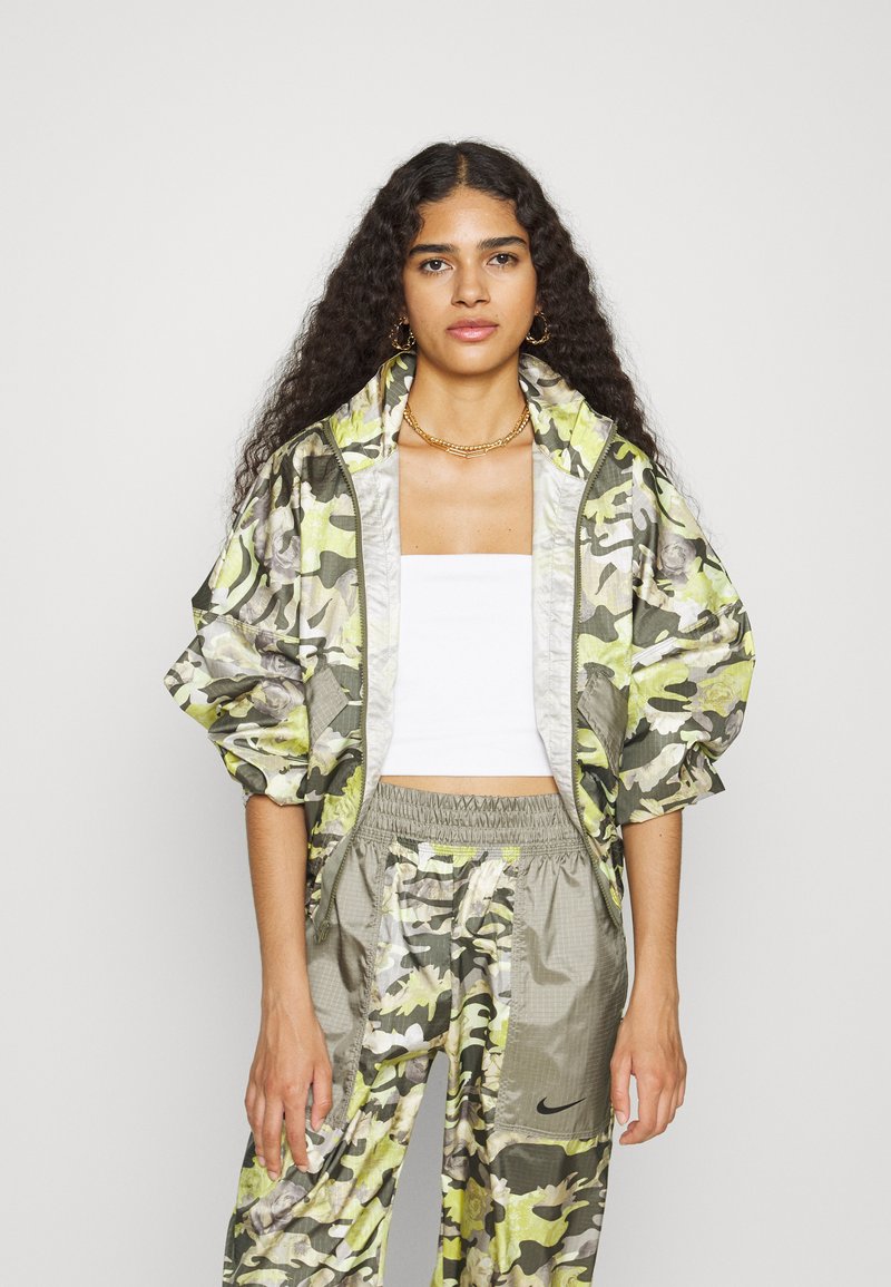 Chándal de camuflaje en tonos verdes y amarillos, que presenta una chaqueta con cremallera y puños elásticos, y pantalones a juego con una cintura elástica.