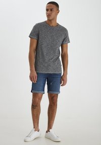 Sivi teksturirani T-shirt s okruglim izrezom, u kombinaciji s plavim denim kratkim hlačama s zavrnutim rubovima. Bijele tenisice upotpunjuju odjevnu kombinaciju.