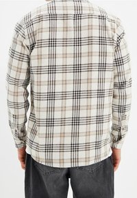 Camicia a maniche lunghe a quadri in beige, nero e crema. Realizzata in un morbido tessuto testurizzato; presenta polsini con bottone e un orlo arrotondato.
