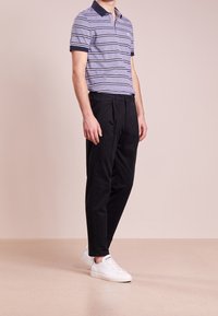 Polo rayé dans des tons de bleu avec col marine, associé à un pantalon noir ajusté et des baskets blanches. Tissu doux avec coupe standard.