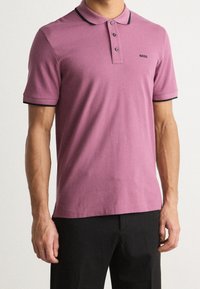 Kortärmad pikétröja i ljuslila bomull med svart krage och svarta ärmslut. Har knapplist och liten logotyp på bröstet.