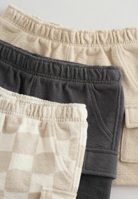 Trois shorts à taille élastique au tissu doux dans des motifs beige, gris foncé et damier beige, disposés en chevauchement sur un fond neutre.