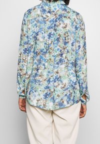 Floral button-up shirt in green, blue, and brown hues. Lightweight fabric with a relaxed fit, featuring long sleeves and a back pleat detail.