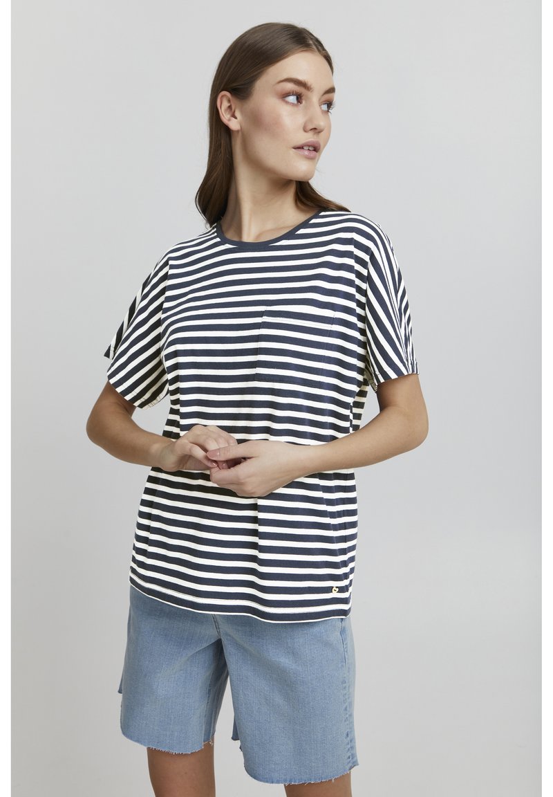 T-shirt w paski w kolorze granatowym i białym z krótkimi rękawami, okrągłym dekoltem i małą kieszonką po lewej stronie, w połączeniu z jasnymi szortami dżinsowymi.