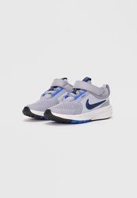 Grijze sportschoenen met blauwe accenten, bovenwerk van mesh, verstelbare banden en een zwarte rubberen zool. Kenmerkt zich door een glad, gebogen ontwerp.