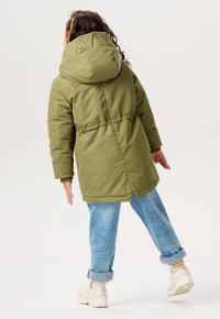 Olivengrønt, polstret jakke med hætte, indsnævret talje og lange ærmer, parret med lys blå oprullede jeans og hvide sneakers.