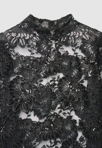 Top in pizzo nero con ricami floreali e paillettes, collo alto e texture trasparente. Motivi floreali dettagliati in tutta la superficie.