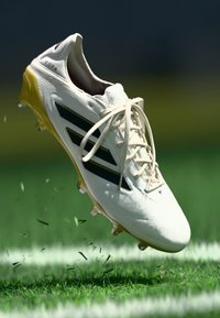 White soccer cleat with black stripes and a yellow sole. Features a textured design on the upper and laces tied at the front.