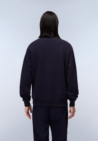 Sudadera azul marino de tejido suave, con mangas largas, puños acanalados y un corte holgado, vista desde la parte posterior.
