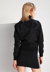 Veste bomber noire avec une finition lisse, des poignets ajustés et un ourlet côtelé. Dotée de poches sur les épaules et de coutures distinctes, associée à une courte jupe noire.