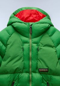 Giacca imbottita verde con cappuccio interno rosso. Presenta una chiusura zip frontale e tasche, tessuto testurizzato e una patch logo nera.