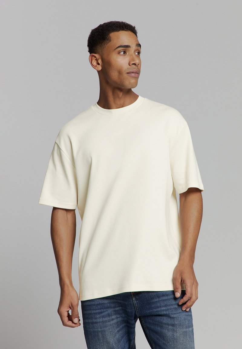 Crème katoenen t-shirt met een relaxte pasvorm, ronde hals en korte mouwen. Gemaakt in combinatie met blauwe denim jeans, met een gladde textuur en een eenvoudig ontwerp.