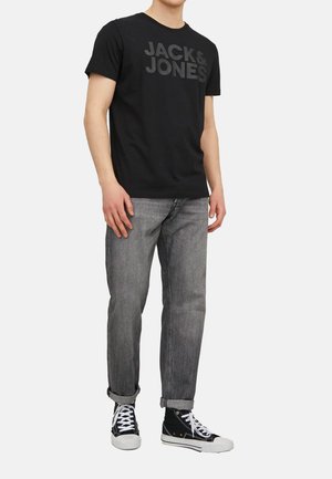 Black cotton t-shirt with "JACK & JONES" logo in dark grey, paired with light grey denim jeans and black canvas sneakers.