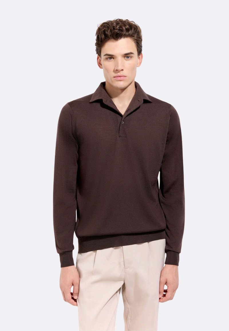 Polo a maniche lunghe marrone con colletto a costine, pattina con un solo bottone e design aderente. Tessuto morbido, abbinato a pantaloni chiari.
