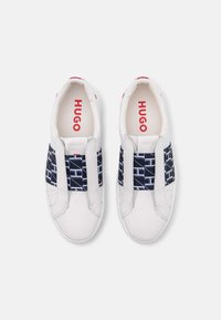 Sneakers bianchi con un elastico blu navy a motivo geometrico, marchio rosso sulla soletta e finitura in pelle liscia.