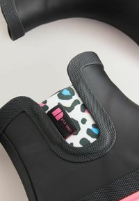 Produit en caoutchouc noir avec une prise texturée, doté d'un intérieur en tissu à motif léopard, rehaussé de couleurs rose et bleue, et d'une étiquette avec "EST 1982."