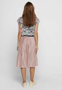 Bloemenprint top met korte mouwen en een cropped model, gecombineerd met een plissée lange, roze rok met een zwarte tailleband. Roomwitte sneakers zichtbaar.