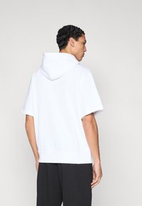 Λευκό φούτερ με κουκούλα και κοντά μανίκια, με άνετη εφαρμογή και ριμπ τελείωμα. Ομαλή υφή υφάσματος και μινιμαλιστικός σχεδιασμός.