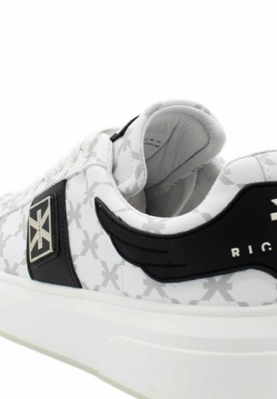 Sneaker bianchi con un motivo testurizzato e accenti neri, dotati di una suola spessa bianca e un logo distintivo sul lato.