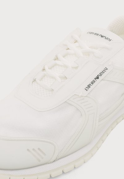 Baskets blanches Emporio Armani avec détails en mesh, lacets blancs et étiquettes de marque sur la languette et sur le côté près des lacets.