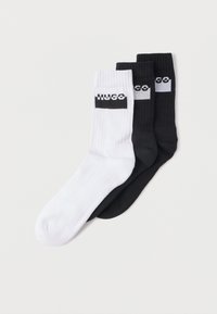 Tres pares de calcetines de algod�ón: uno blanco, uno negro y uno gris, con textura acanalada y el logo HUGO en negro sobre fondo blanco.
