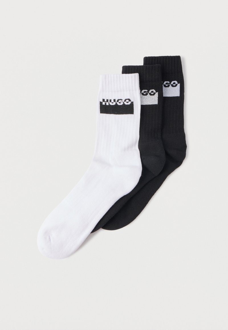 Tres pares de calcetines de algodón: uno blanco, uno negro y uno gris, con textura acanalada y el logo HUGO en negro sobre fondo blanco.