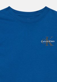 Mėlynas medvilninis marškinėliai su apvalia iškirpte, su mažuoju sidabriniu Calvin Klein logotipu kairėje krūtinės pusėje. Lygus tekstūra, reguliaraus kirpimo.